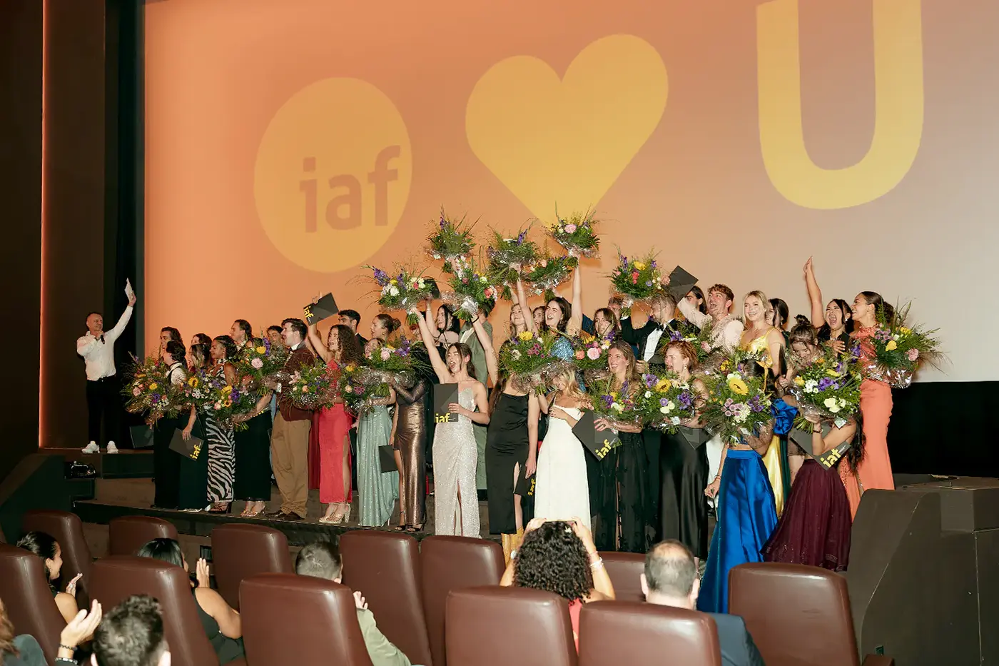 Abschlussjahrgang jubelt mit Blumensträußen auf der Bühne, IAF Abschlussfeier 2024 in Köln