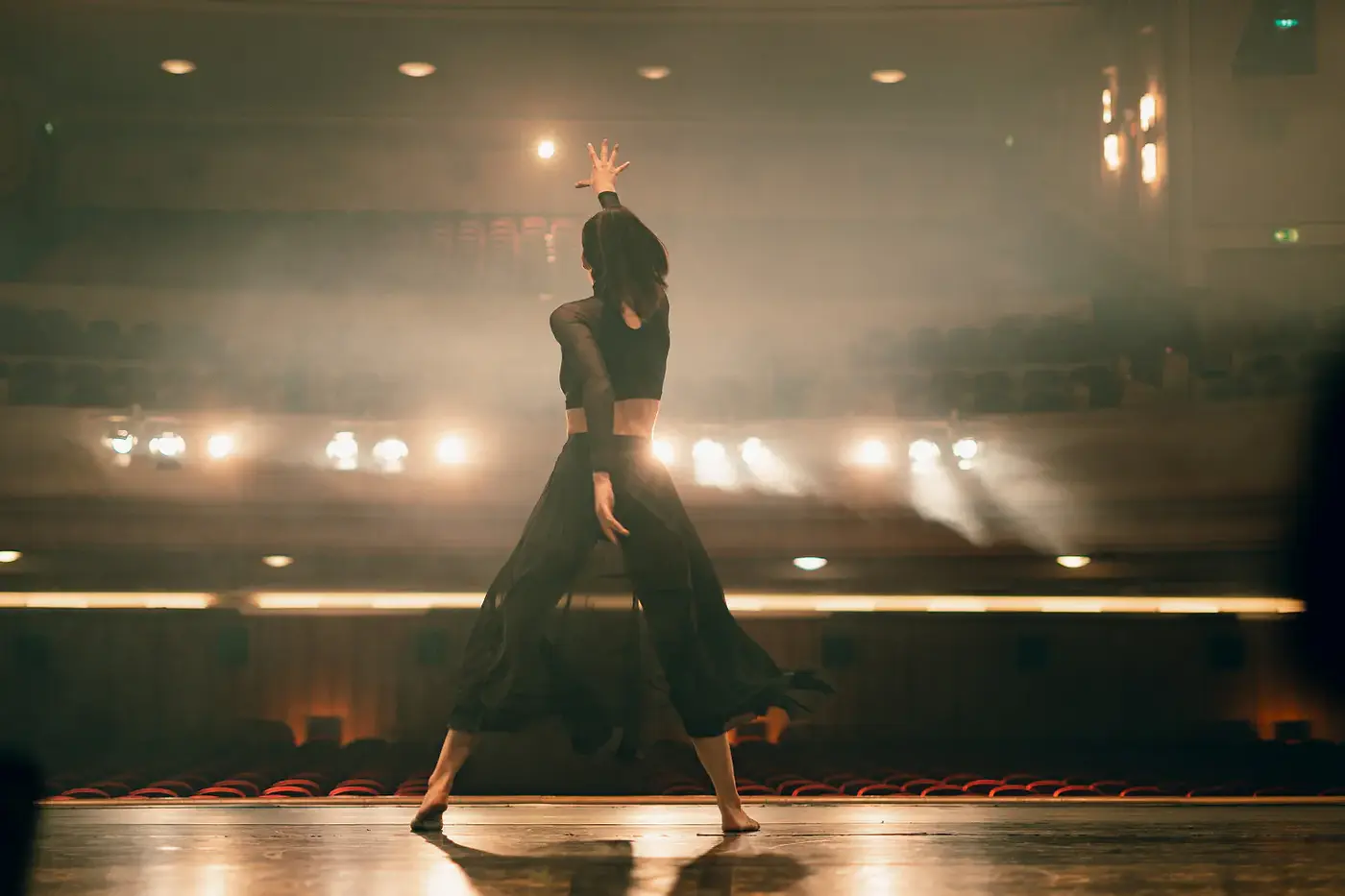 Tänzerin von hinten auf einer Theaterbühne mit erhobenem Arm, Standbild aus dem IAF Abschlussfilm Portugues Dancing 2025