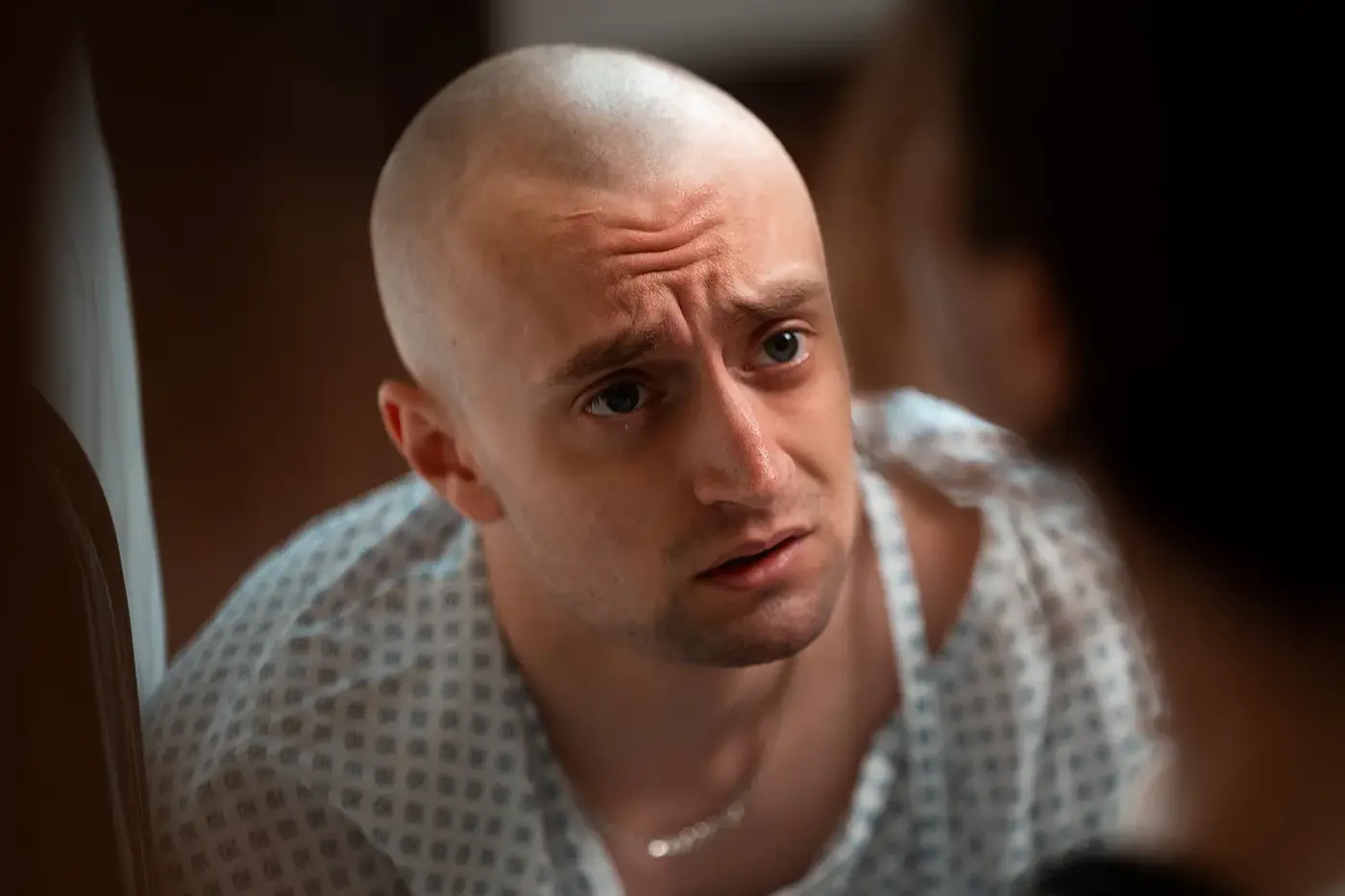 Nahaufnahme eines jungen Mannes im Patientenhemd mit sorgenvollem Blick, Standbild aus dem IAF Abschlussfilm Junky Breakup 2025